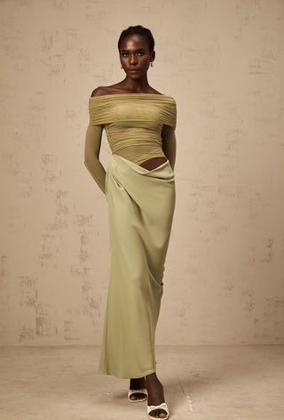 Woman wearing a green off-shoulder top and long skirt against a beige background