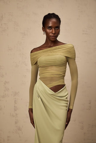 Woman wearing a green off-shoulder dress against a beige background
