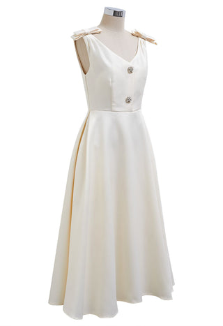 Elegant white midi dress with bow shoulder details, crystal buttons, and side pockets, perfect for bridal showers, engagement parties, rehearsal dinners, and cocktail events. A-line silhouette ideal for bridal and cocktail events. Cielie Vienna Fashion Brand Rental Gown