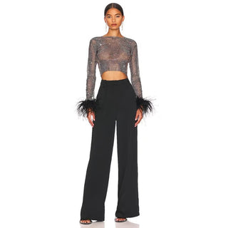 Woman wearing a sheer top with feathered cuffs and black pants on a white background