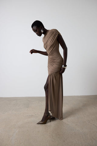 Woman wearing a brown dress standing against a white wall.