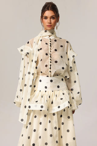Woman wearing a polka dot dress with a sheer overlay on a plain background