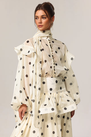 Woman wearing a cream-colored polka dot dress with a plain background