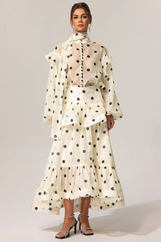 Woman wearing a polka dot dress with sheer sleeves on a plain background