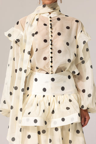 Woman wearing a cream polka dot dress with a sheer overlay against a neutral background