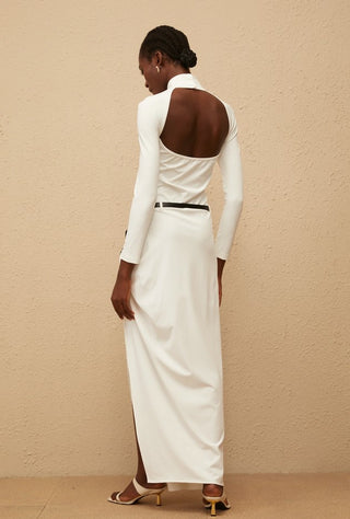 Woman wearing a white long-sleeve dress with a high neckline against a beige wall.