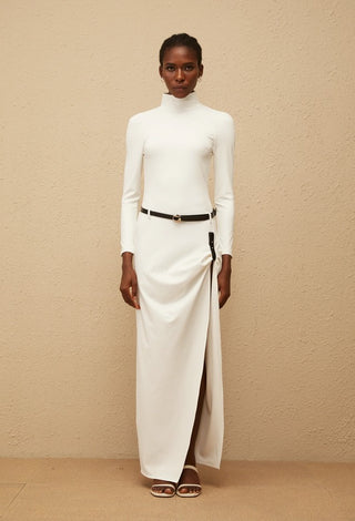 Woman wearing a white turtleneck dress with a black belt against a beige background