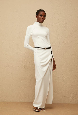 Woman wearing a white turtleneck and cream-colored pants against a beige background