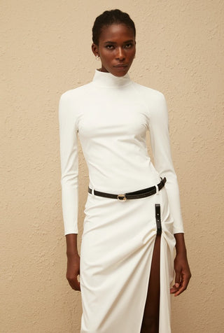 Woman wearing a white turtleneck dress with a black belt against a beige background