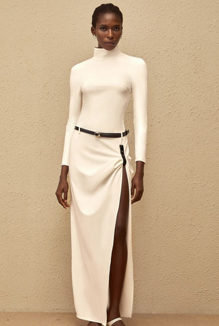 Woman wearing a white long-sleeve top and high-split skirt against a beige background