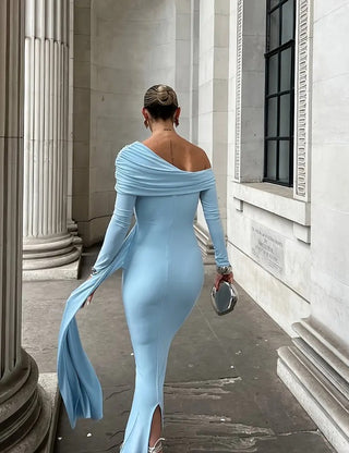 Person wearing a light blue off-shoulder dress walking past classical columns.